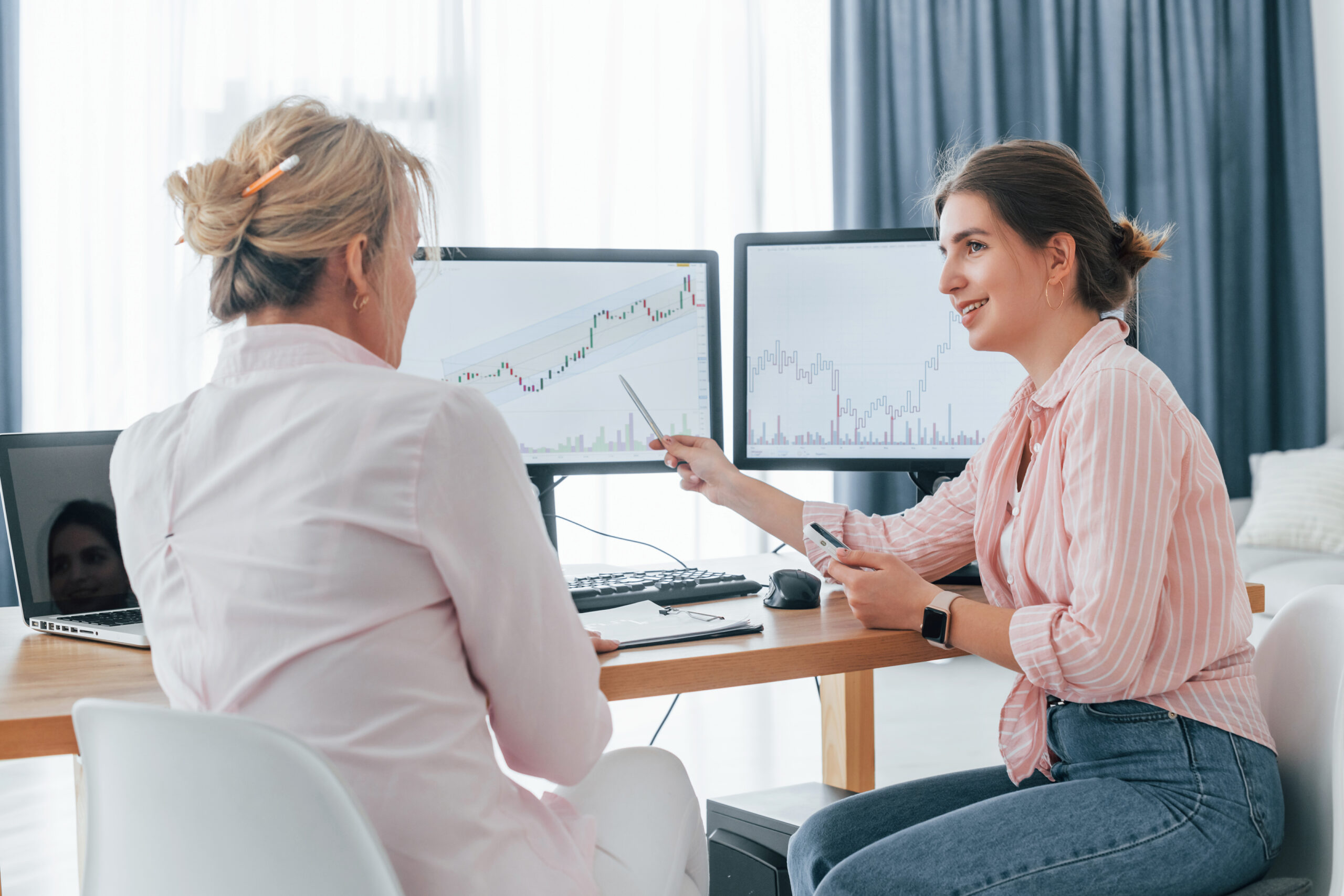 talking with each other. two female stock brokers in formal wear is working in the office by pc